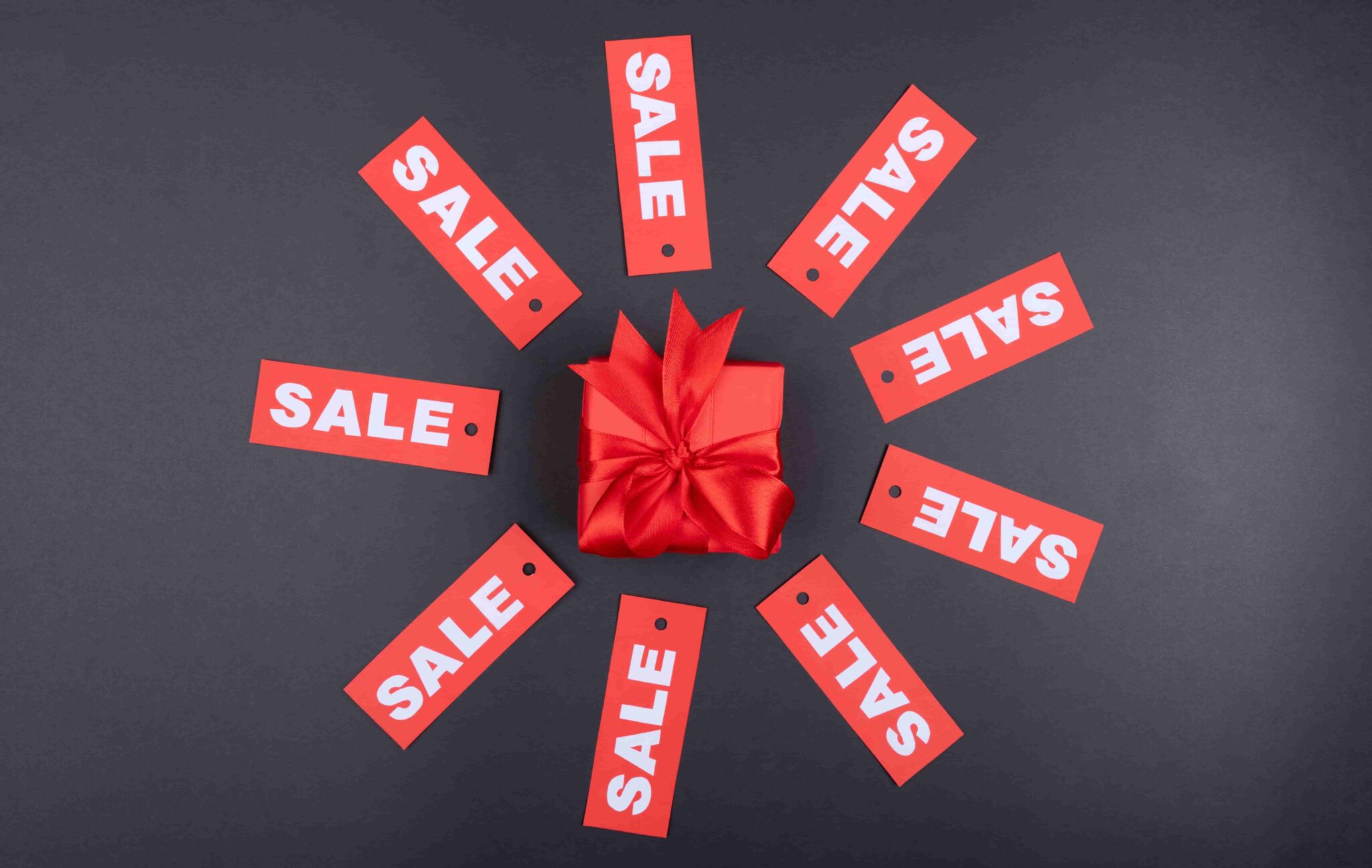 Red sale tags surrounding a wrapped gift on a dark background